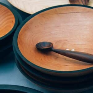 Große Holzschale mit dunklem Rand und passendem Holzlöffel, gestapelt mit weiteren Schalen im Hintergrund.